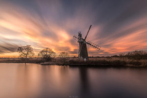 How hill on the Norfolk broads during a photography workshop at sunset with a fire red sky and refelction on the water